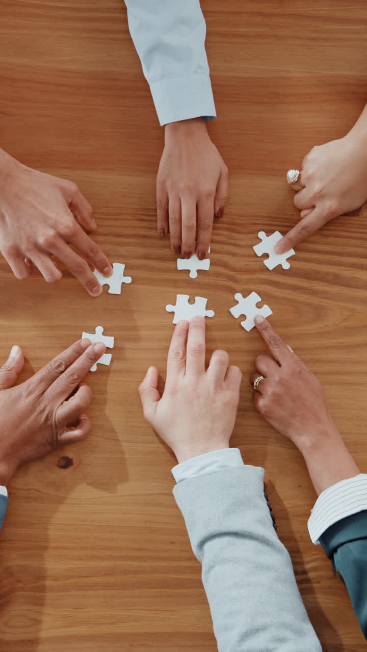 Gruppo di mani che assembla pezzi di puzzle su un tavolo di legno