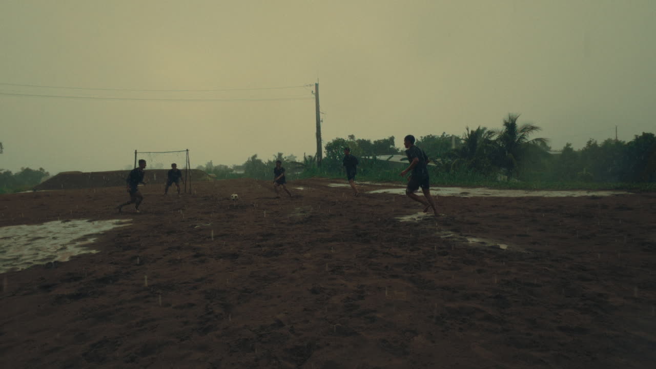 Wet football match in slow motion, players running on muddy field during rainfall