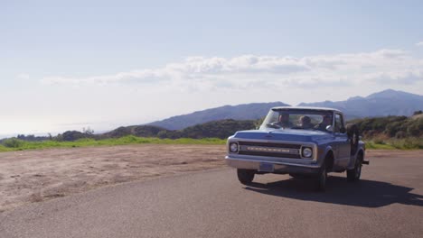 A-group-of-friends-in-a-blue-pickup-truck-drive-on-a-rural-road-2