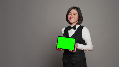 asian receptionist holding tablet with greenscreen on camera,