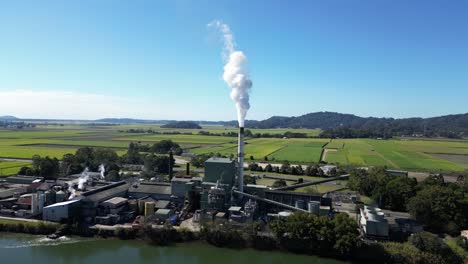 smoke billows from a sugar mill refinery on the banks of a country river with a mountain backdrop view