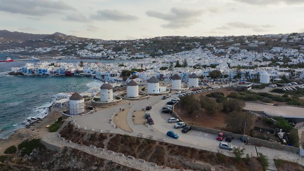 Ripresa drone panoramica lenta dei mulini a vento dell'isola di Mykonos e di Piccola Venezia all'alba, Cicladi, Grecia. Nuvole sparse, luce dorata del mattino