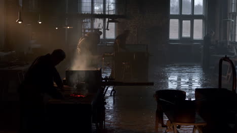 blacksmiths working in a dark, atmospheric forge or metalworking workshop