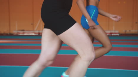 close up of legs of two multiethnic female athletes running together on an indoor track