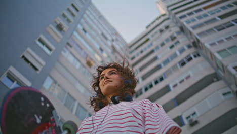 skateboard girl standing city building bottom view closeup. curly hipster posing