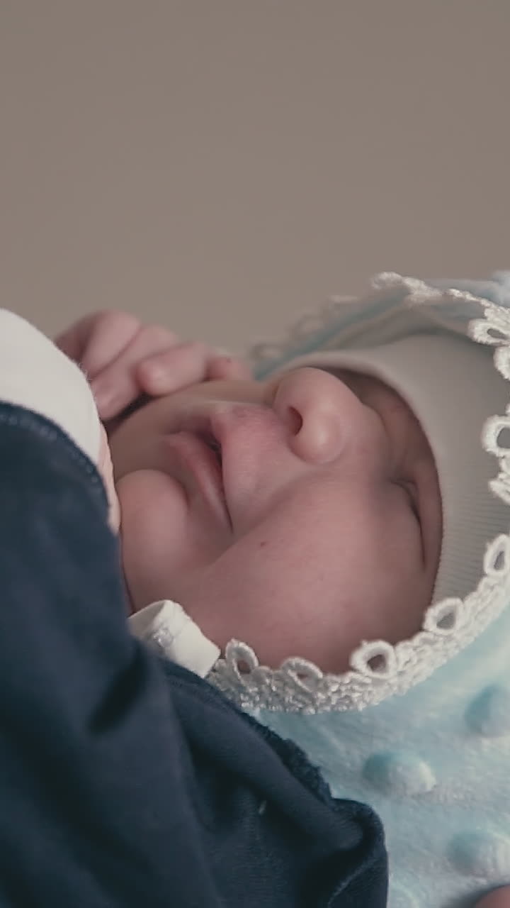 happy young father in grey sweatshirt holds cute newborn son in tuxedo and warm hat at light wall extreme close view