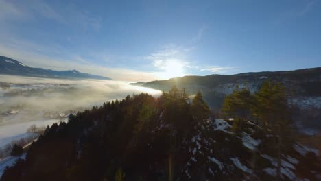 fpv drone shot, the landscape covered under the fog with surrounding mountains in the morning at winter time in slovenia captured in 4k, drone flying fast, close to objects with lots of movement