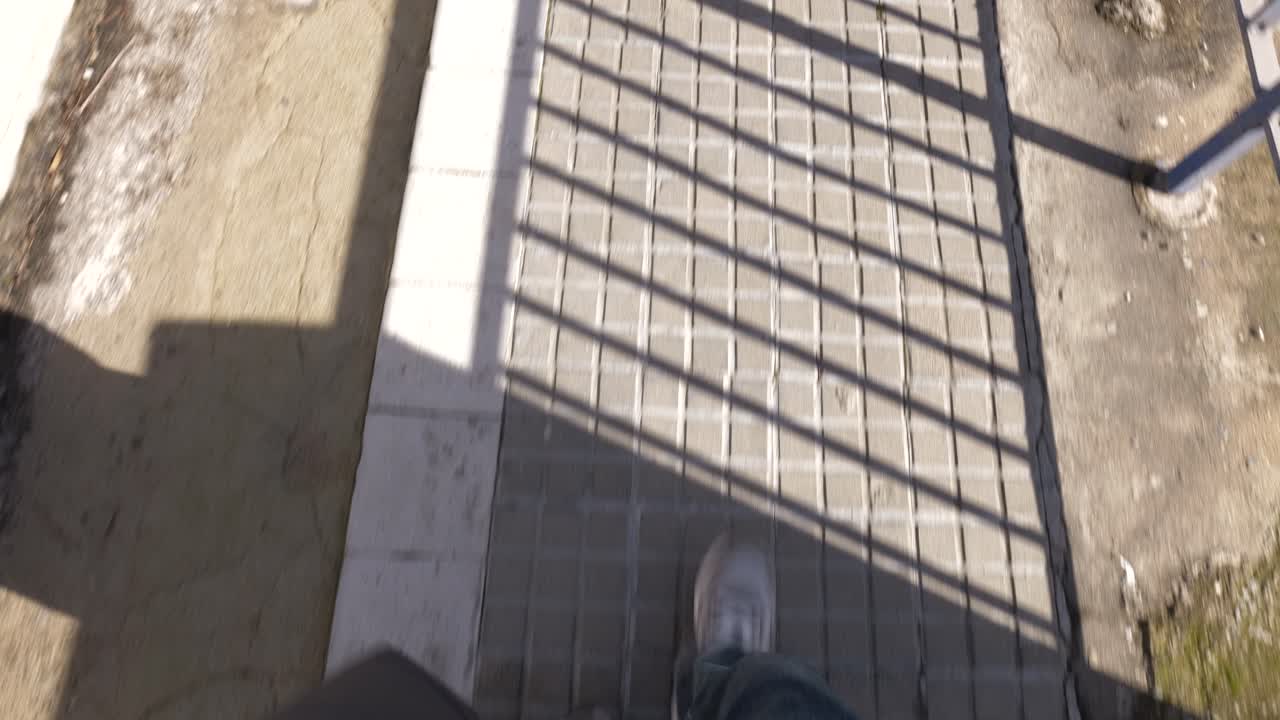 Toma en primera persona de una persona caminando por la acera en una calle de la ciudad durante el día
