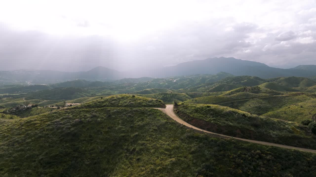Aerial photo of a rural gravel road cutting through the scenic hills of Marbella, Andalusia, surrounded by greenery and mountains.