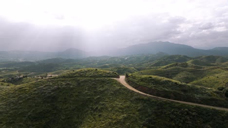 aerial photo of a rural gravel road cutting through the scenic hills of marbella, andalusia, surrounded by greenery and mountains.