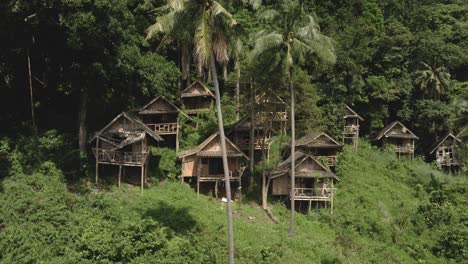 pan up shot of ramshackle bamboo backpacker huts on a hill in the jungle in thailand