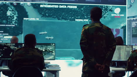 Staff-sergeant-monitoring-satellite-live-imagery-on-a-big-screen