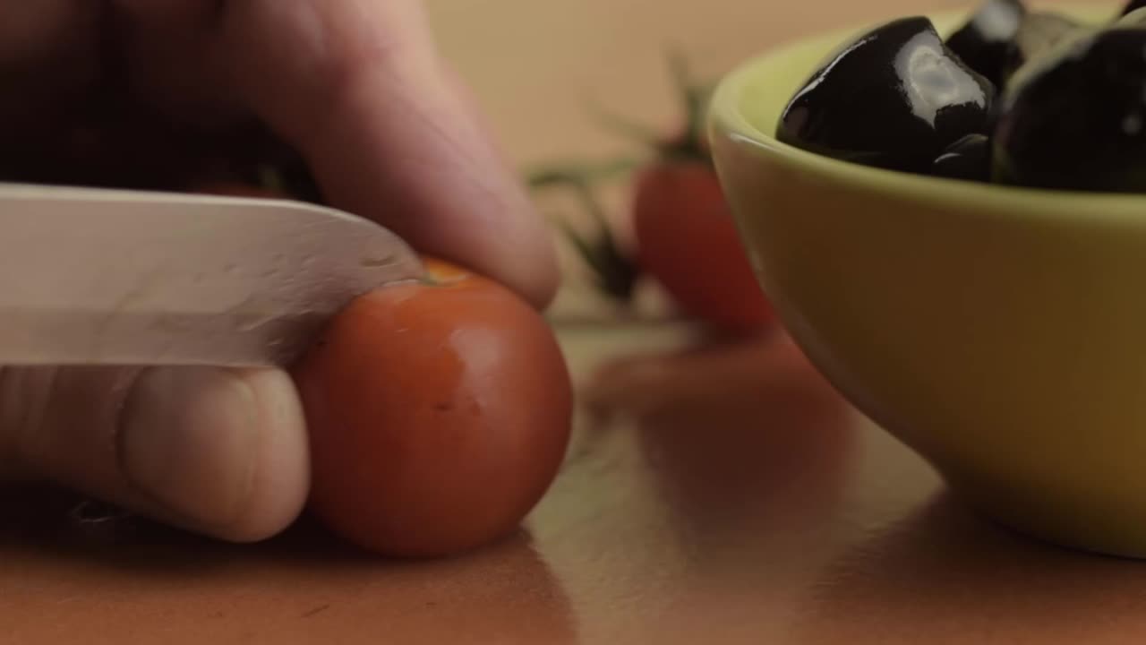 Hand slicking cherry vine tomatoes with black olives close up shot