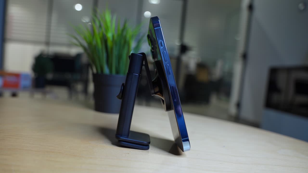 Hand placing smartphone on a magnetic desk mount in a modern workspace. Great for tech tutorials, gadgets, mobile accessories, or desk setups.