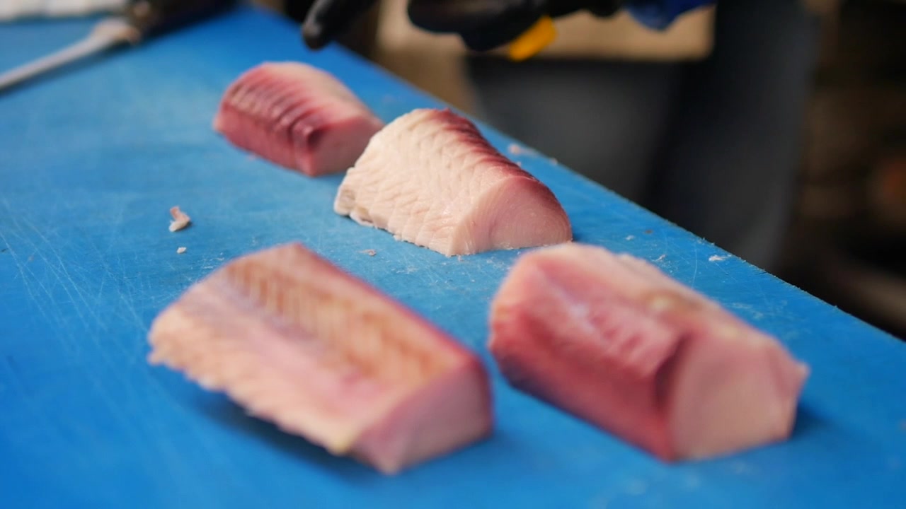 Nærbillede af hænder, der udbener frisk fiskefilet på et blåt skærebræt.