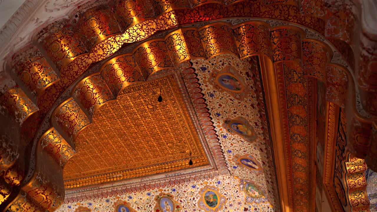 Una ripresa statica ravvicinata che guarda verso l'alto il magnifico soffitto a foglia d'oro e i dettagli ad arco finemente dipinti dell'interno del Phool Mahal nel Forte di Mehrangarh, Jodhpur, Rajasthan, India.