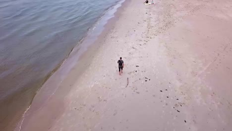 aerial shot of man walking on sandy beach on a cloudy day