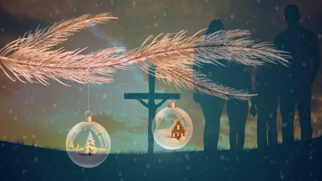 hanging christmas ornaments from branch with cross and silhouettes in background