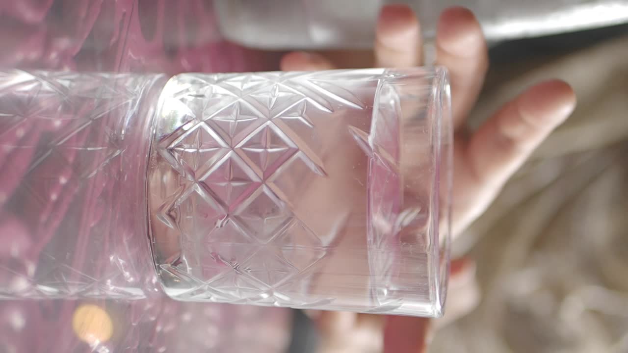 Hand holding a cut glass water tumbler on a table