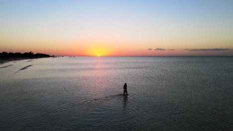 wide angle drone shot of a beautiful young women walking in the shallow water off the beaches during sunset of the tropical island of holbox in mexico shot in 4k
