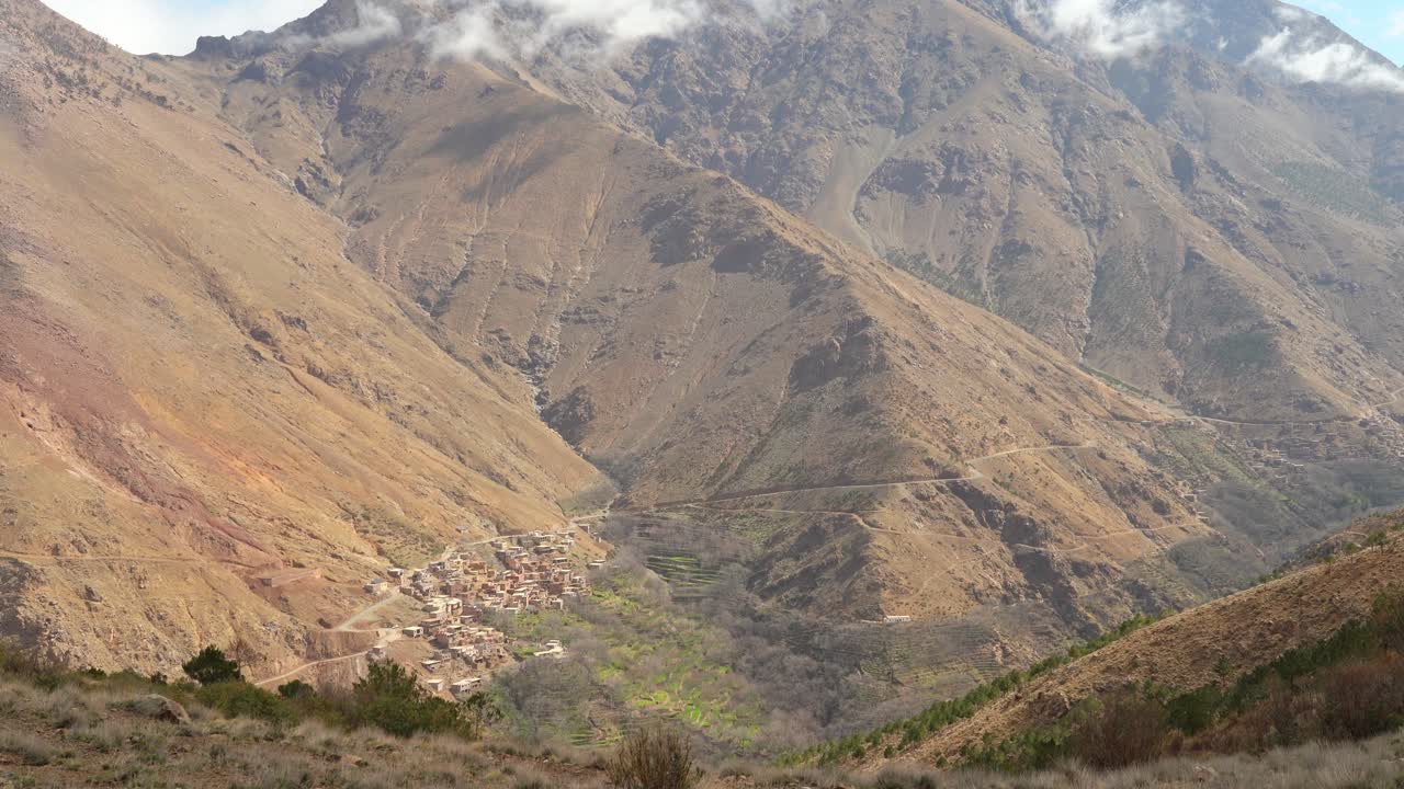 The village’s stone houses blend with the beauty of surrounding hills and rugged gorges, all bathed in midday sun beneath the snow-covered Toubkal Mountain in Morocco