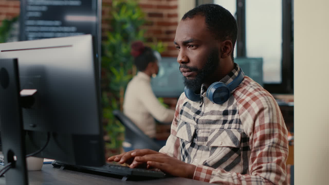 Portrait of focused african american programer wearing wireless headphones working looking at computer screen