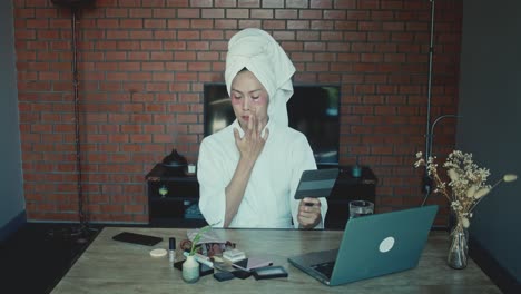 woman doing makeup tutorial on laptop at home