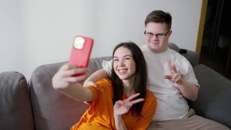 síndrome de down hombre sentado en el sofá con una chica, hacen una selfie juntos