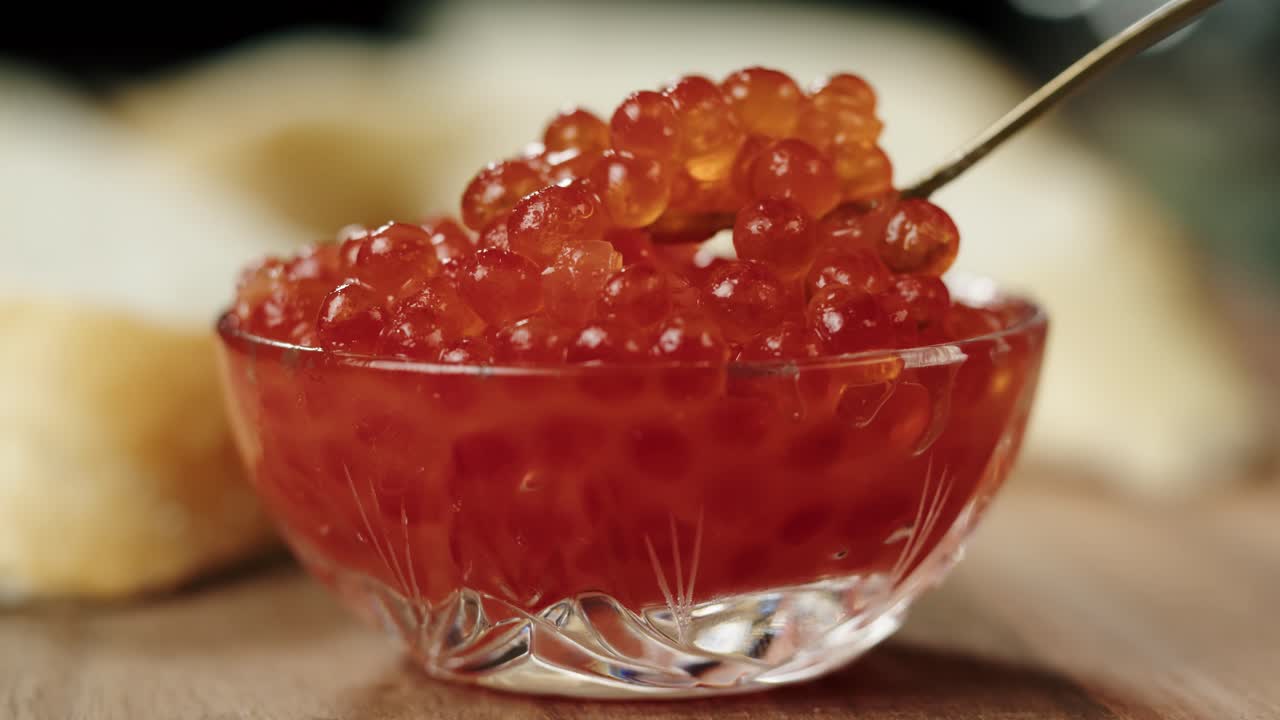 Primo piano di caviale rosso in una ciotola di vetro, raccolto con una forchetta