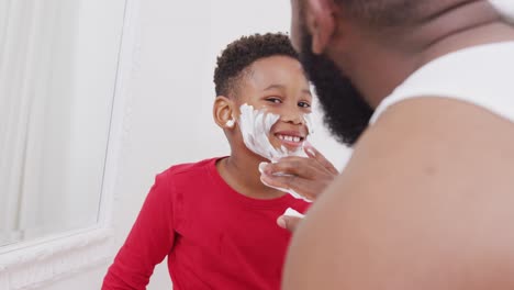 padre e hijo afroamericanos felices aplicando crema de afeitar en la cara en el baño, en cámara lenta