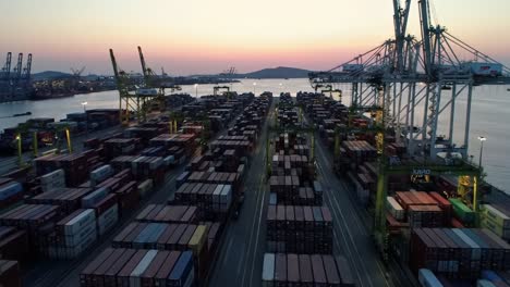 aerial view of docked shipping containers at dusk, showcasing a busy port with cranes and a serene water landscape under a twilight sky