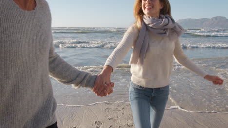 Pareja-Divirtiéndose-Corriendo-Juntos-Por-La-Playa-De-Invierno