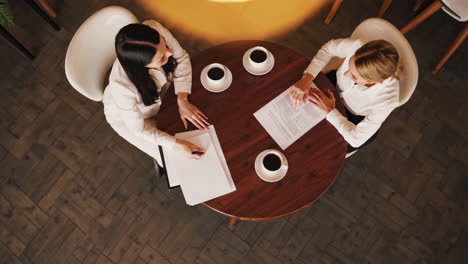 two businesswomen discussing documents over coffee in a cafe