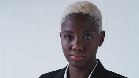 portrait of determined young businesswoman wearing suit standing against white studio wall