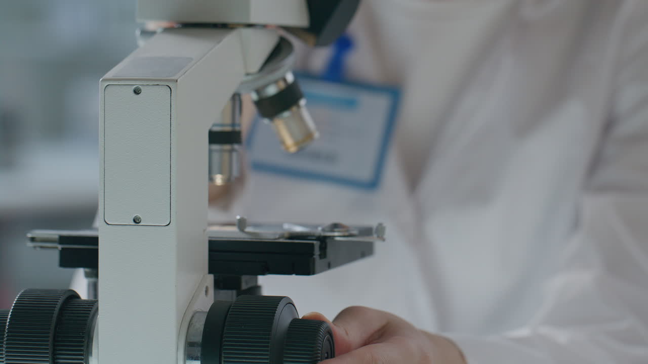 Female Lab Scientist Using Focus Knob as Looking through Microscope