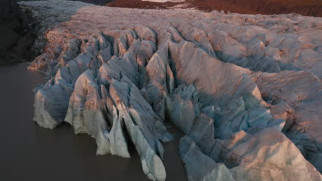 tilting aerial of glacier with close up of ice whilst revealing mountains