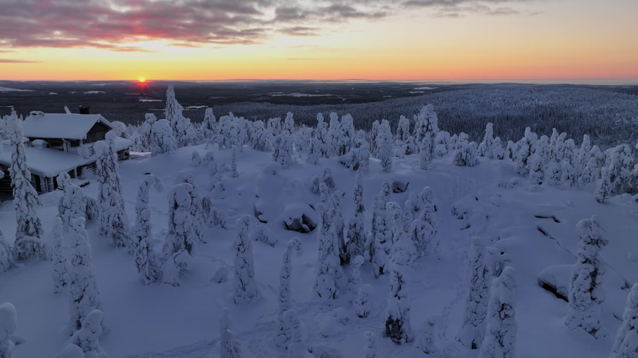 Luftsporing med tilt-opptak av et hus og snødekt villmark, solnedgang i Lappland
