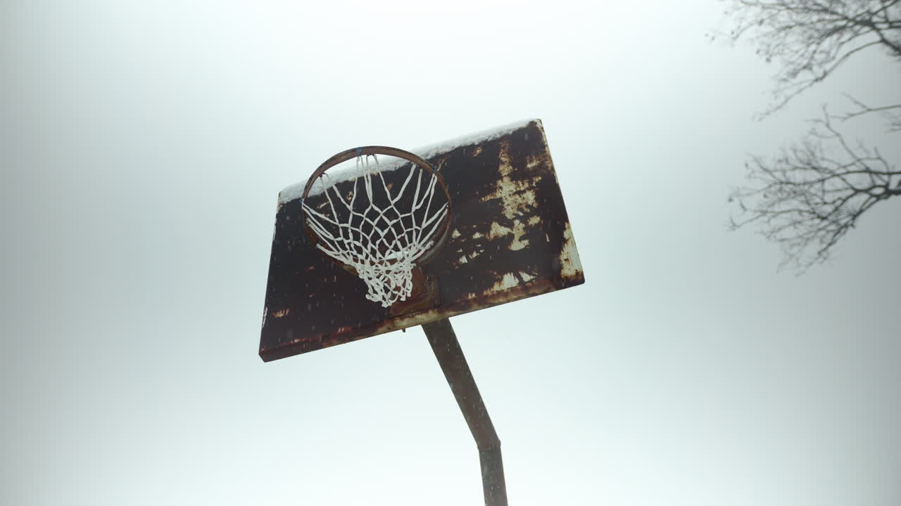 viejo anillo de baloncesto oxidado con copos de nieve en cámara lenta cayendo durante la tormenta de nieve de invierno