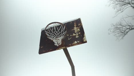 old, rusty basketball hoop with slow motion snowflakes falling during winter snow storm