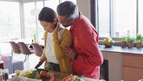 pareja feliz diversa cocinando juntos, cortando verduras y abrazándose en la cocina