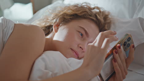 morning girl using cellphone on bed pillow. closeup serene blonde check mobile