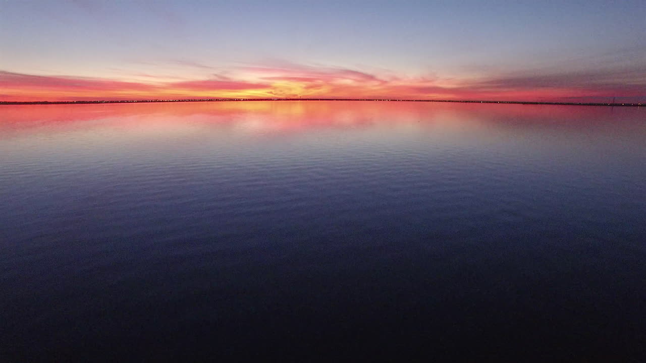 Aerial push in and pan up revealing shot of sunset over a calm lake.