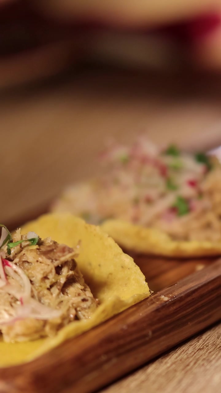 Hånd tager en frisk carnitas-taco fra et træbræt