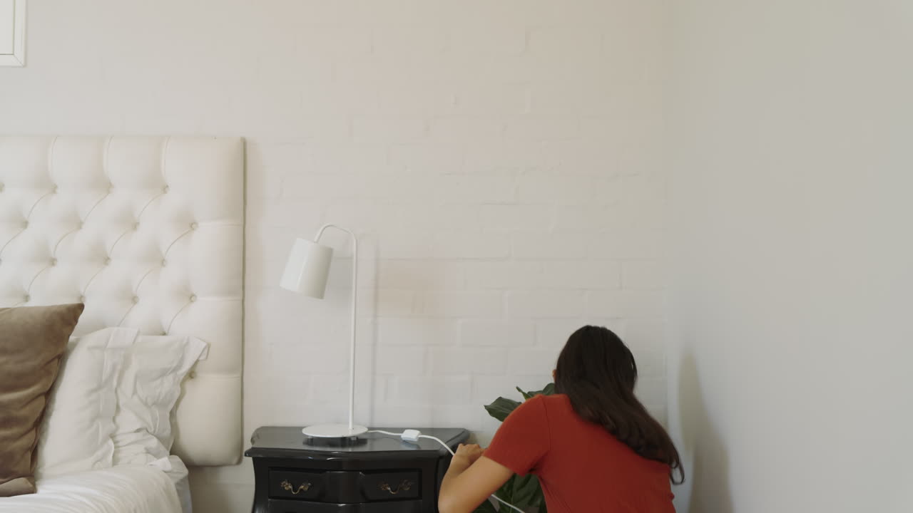 Woman in bedroom smiling while adjusting lamp on bedside table, at home
