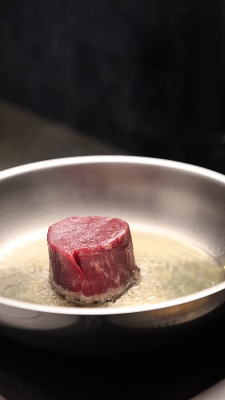 Bistecca cruda che sfrigola nell'olio bollente in una padella