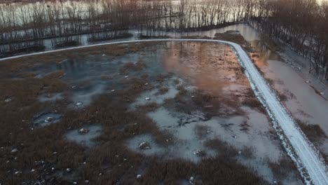 Aerial-Shot-of-Frozen-Icy-Winter-Landscape-with-tress,-lakes,-ponds-and-road-at-sunrise