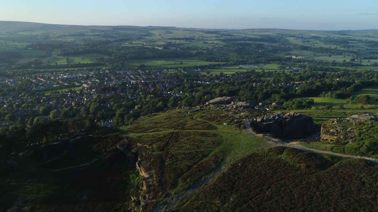 establecimiento de disparos de drones sobre la parte posterior de las rocas de vaca y ternero con vistas al valle con la ciudad balneario de ilkley en un día soleado de verano a la hora dorada west yorkshire, reino unido
