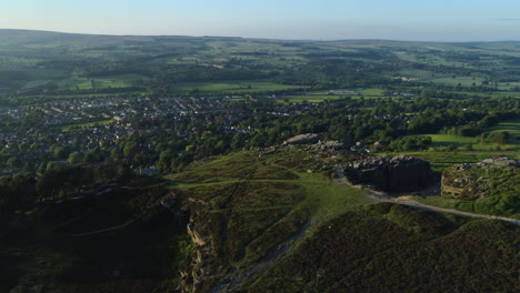 Establecimiento-De-Disparos-De-Drones-Sobre-La-Parte-Posterior-De-Las-Rocas-De-Vaca-Y-Ternero-Con-Vistas-Al-Valle-Con-La-Ciudad-Balneario-De-Ilkley-En-Un-Día-Soleado-De-Verano-A-La-Hora-Dorada-West-Yorkshire,-Reino-Unido