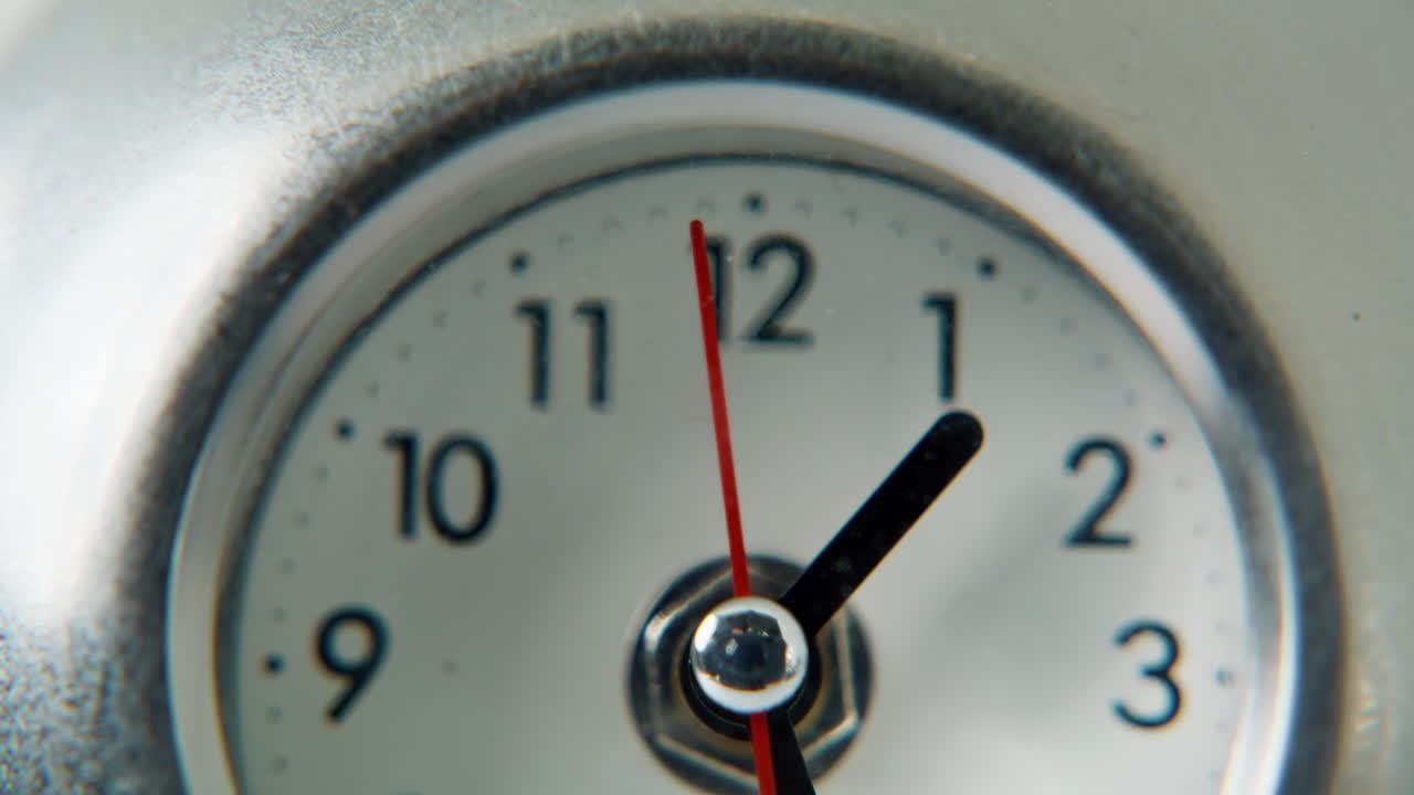 Closeup round clock dial with black numbers. Red little arrow running on circle
