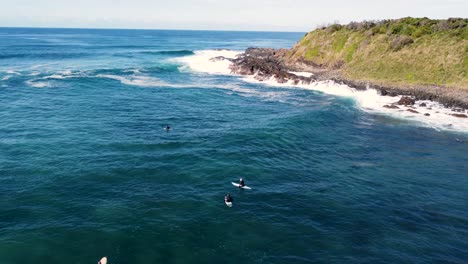 drone aerial still shot of surfers waiting in line-up on headland coastline point break surfing beautiful landscape tourism old bar point taree nsw australia 4k